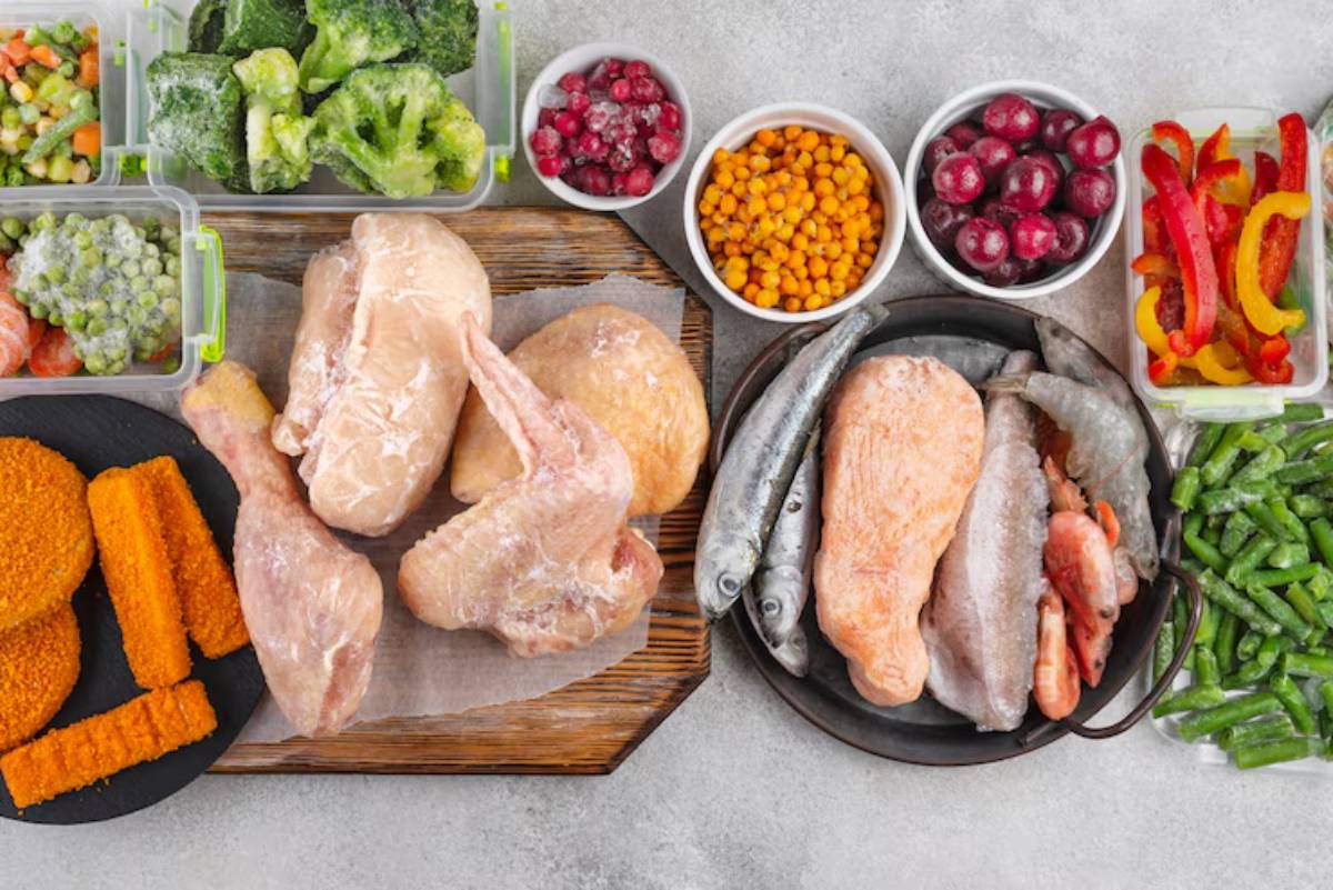 A variety of frozen meats and vegetables displayed: chicken, fish, shrimp, and colorful vegetables in bowls and containers.