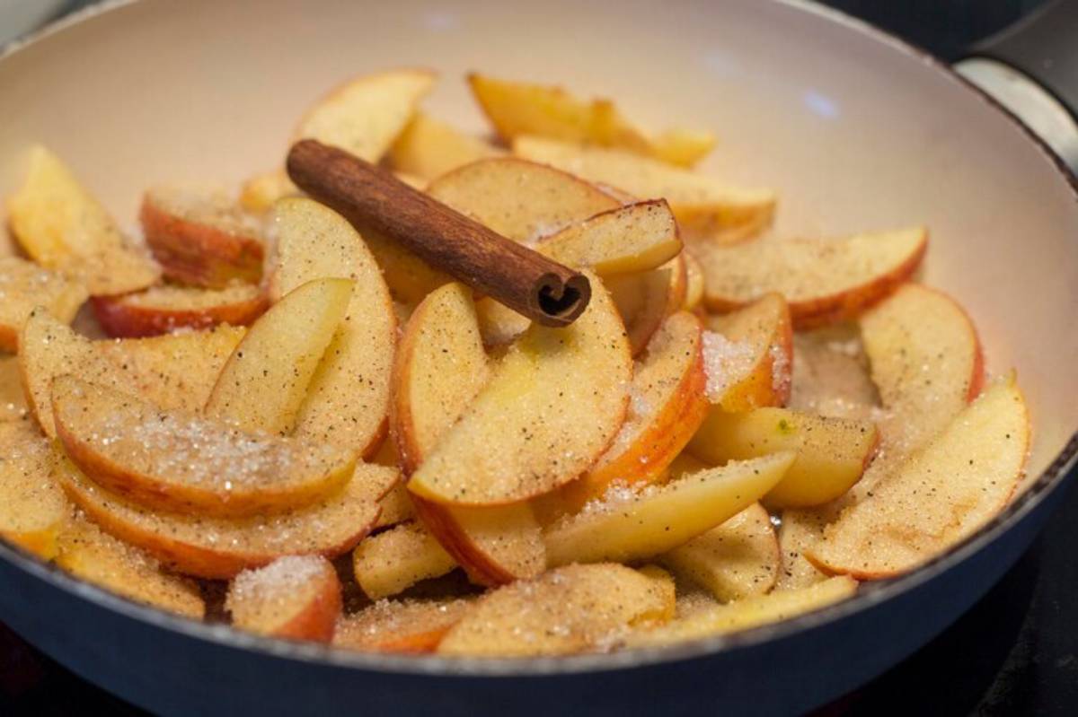 Sliced apples seasoned with sugar and cinnamon in a skillet, ready for cooking.