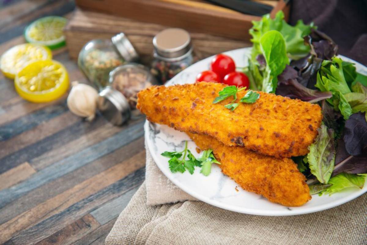 Crispy fried fish fillets served on a white plate with fresh salad greens and cherry tomatoes, garnished with parsley.