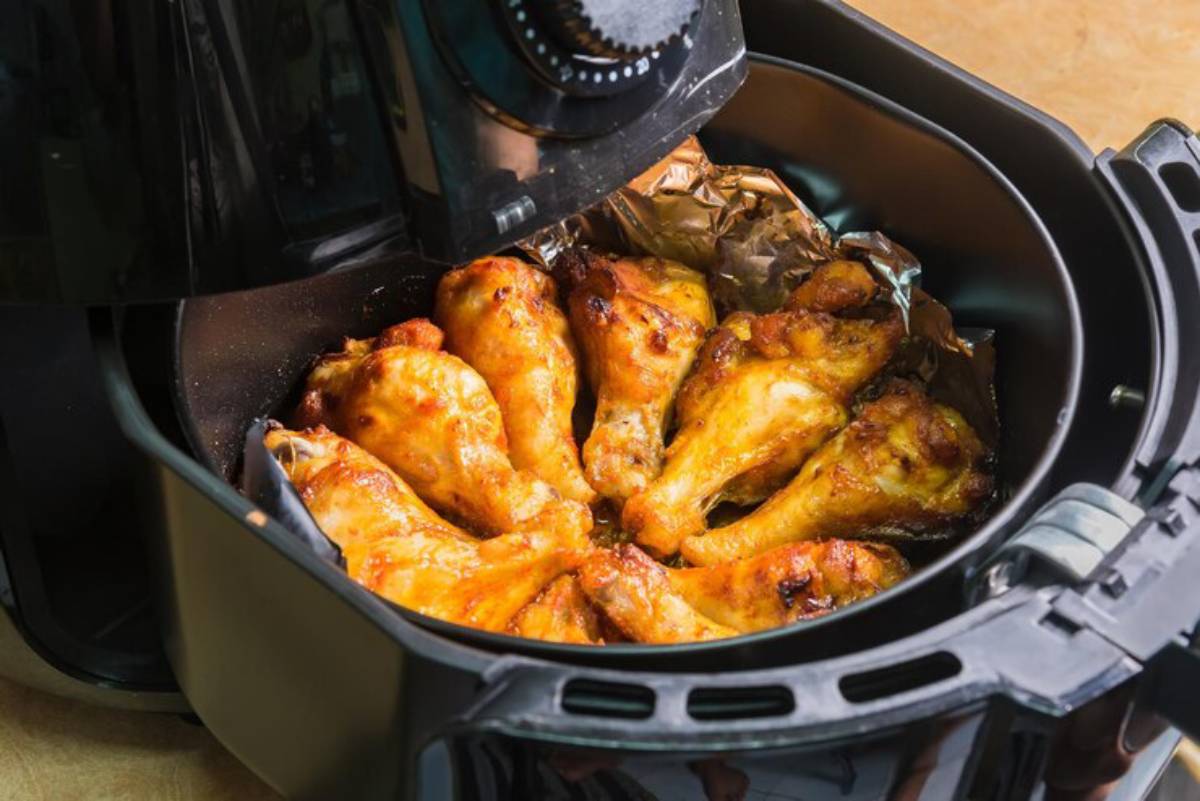 Crispy, golden-brown chicken drumsticks in an air fryer, with the lid slightly open, revealing the delicious food inside.