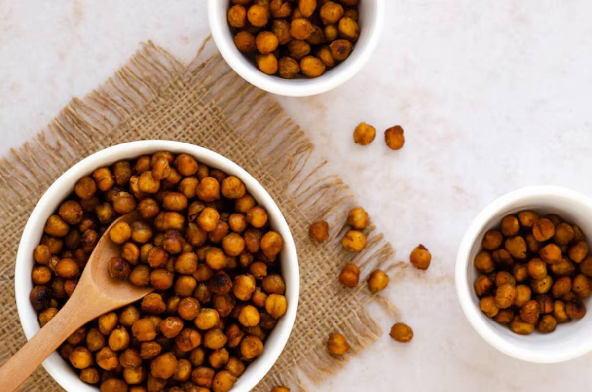Close-up of crispy roasted chickpeas in white bowls with a wooden spoon, arranged on burlap, against a light backdrop.