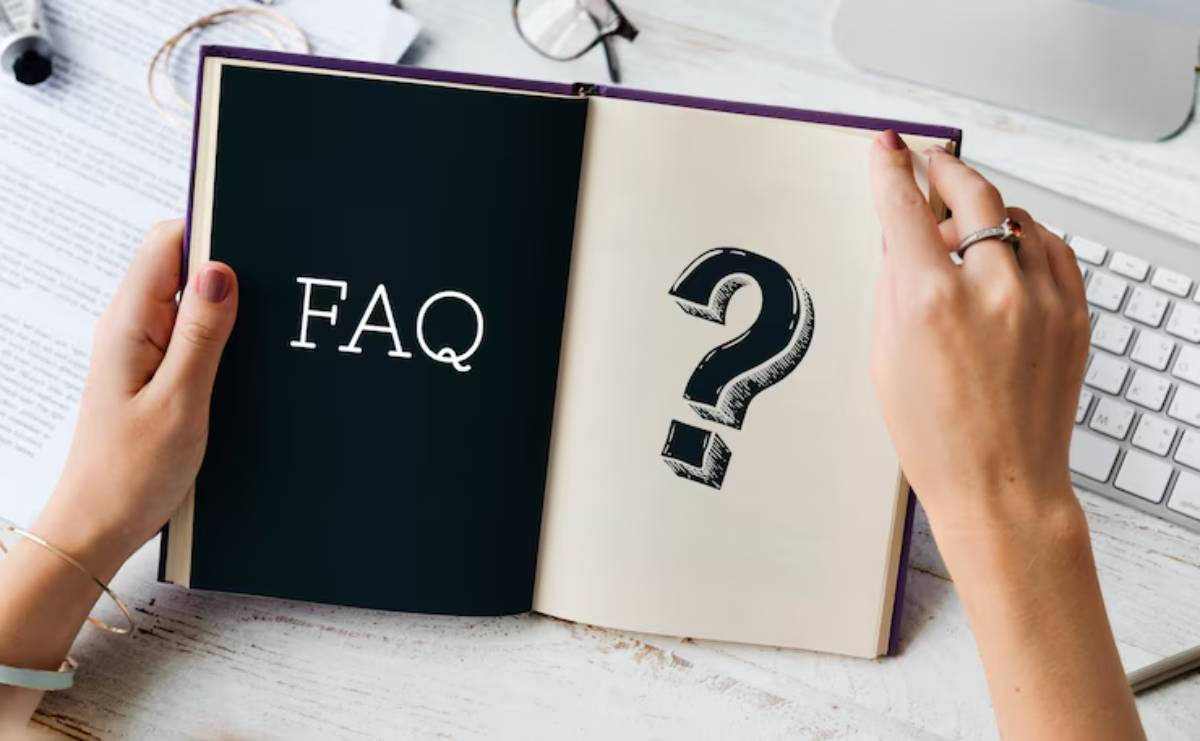 A person holding an open book displaying FAQ and a large question mark, with office supplies in the background.