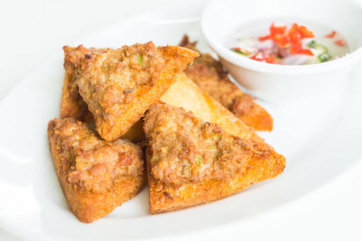Three golden-brown, triangular fritters served with a small bowl of dipping sauce adorned with diced vegetables.