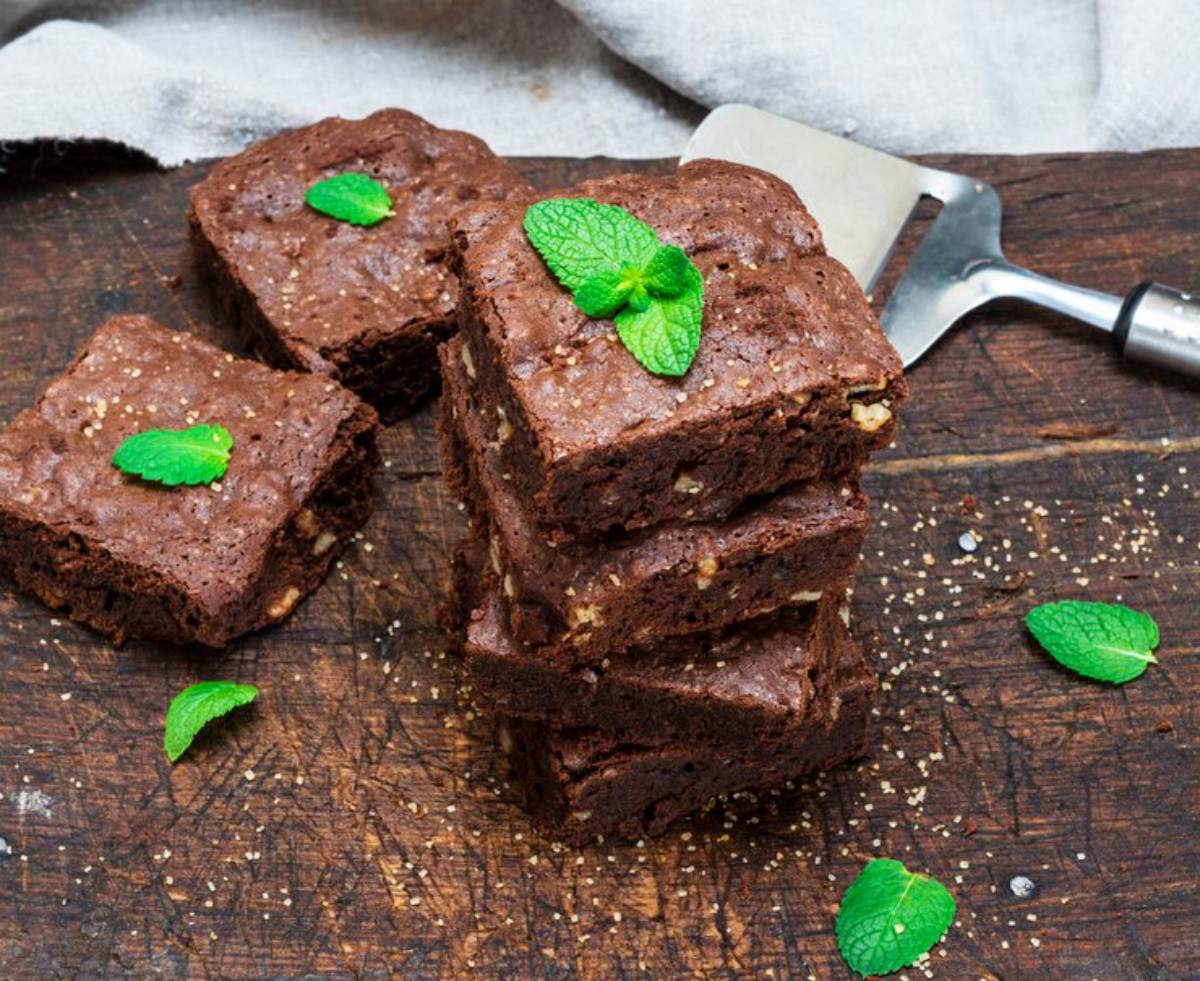 A stack of rich chocolate brownies garnished with mint leaves on a wooden cutting board, with a metal spatula beside them.