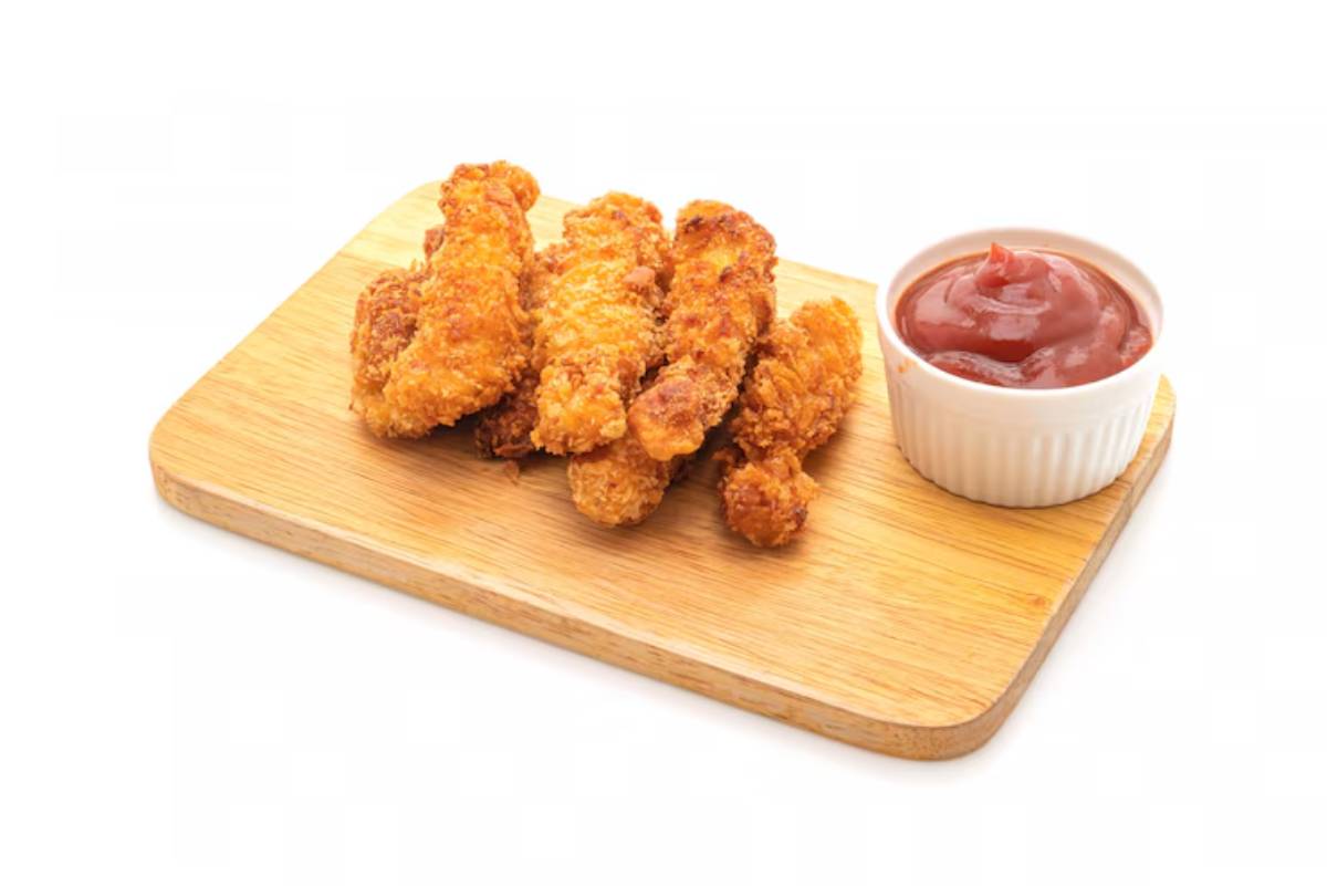 A wooden serving board holds crispy golden chicken strips alongside a small bowl of rich red ketchup. 