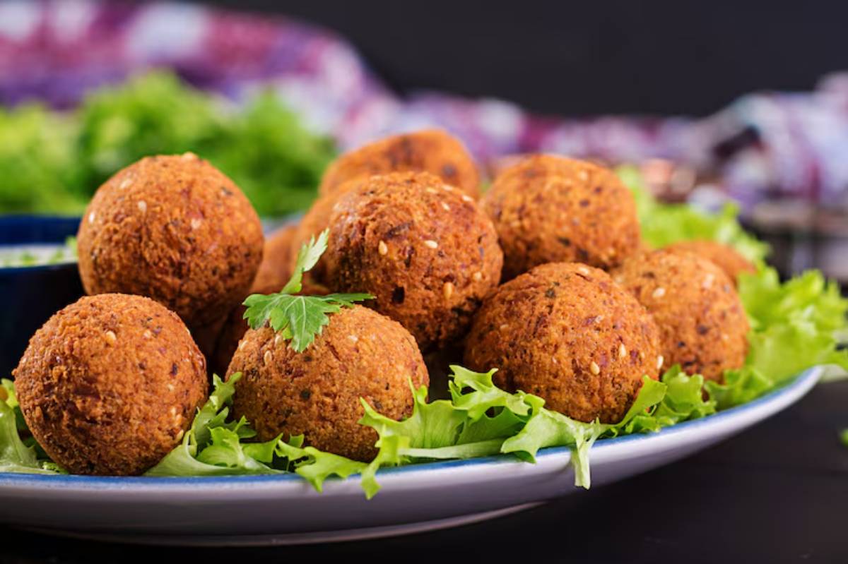 A plate of crispy, golden-brown falafel balls garnished with fresh lettuce and herbs, set against a dark background.