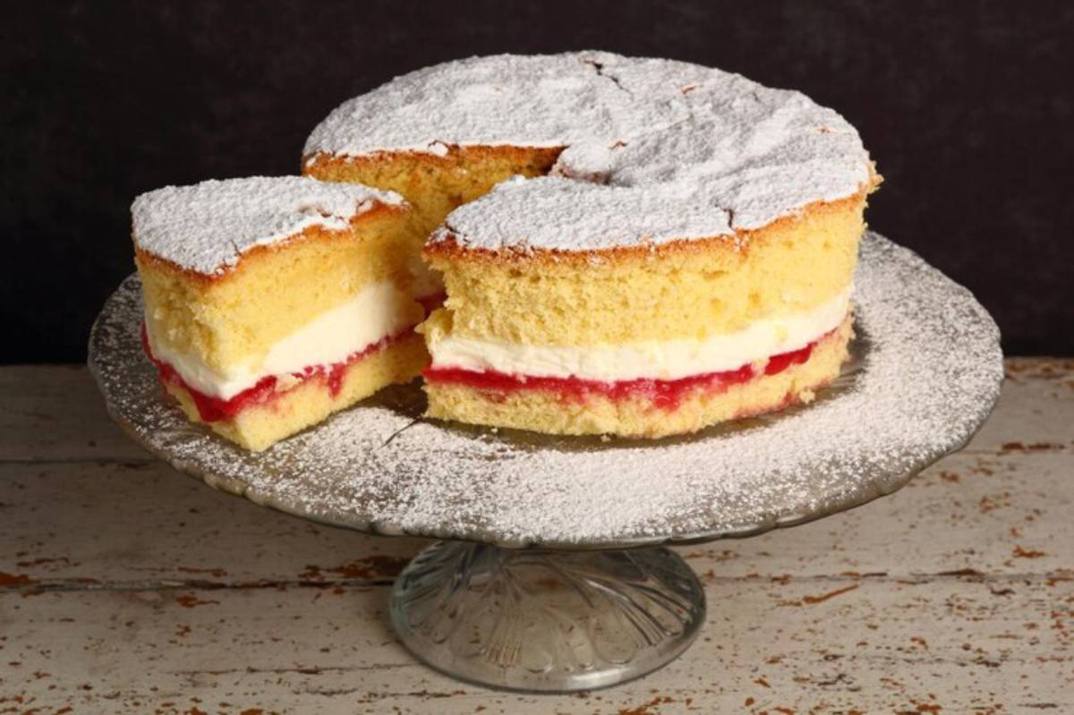 A light and fluffy sponge cake dusted with powdered sugar, featuring layers of cream and raspberry jam, with a slice removed.