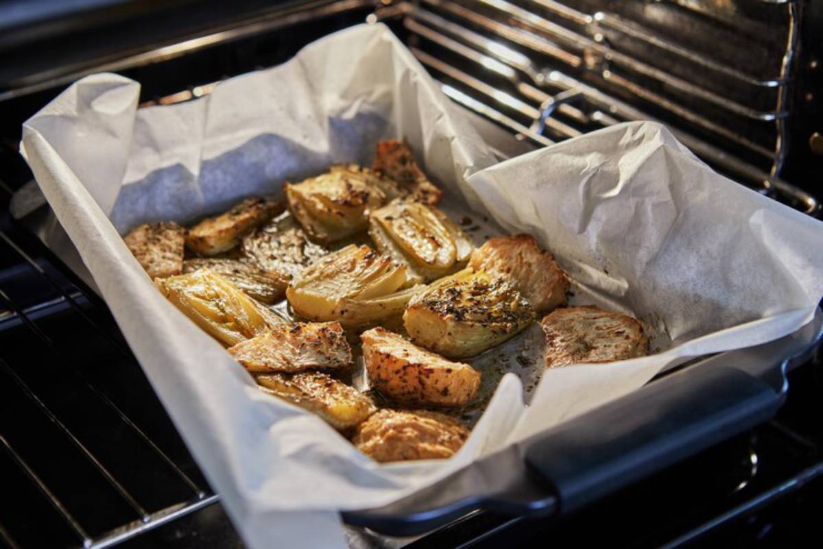 Roasted vegetables including caramelized fennel and potatoes on parchment paper in a baking tray in the oven.