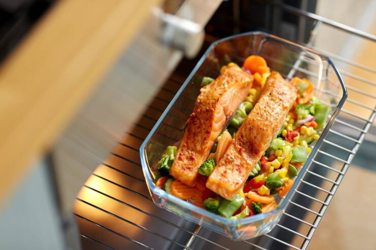 Two seasoned salmon fillets on a bed of mixed vegetables in a glass baking dish, placed inside an oven.
