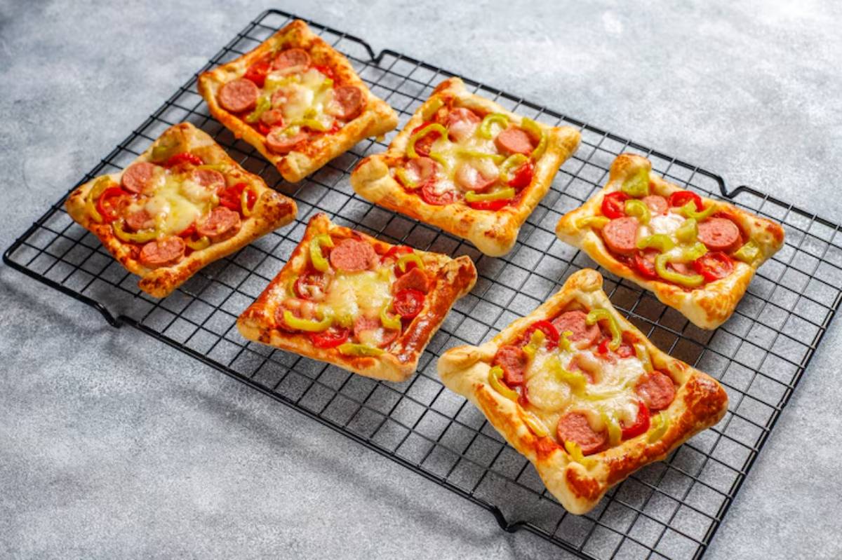 An overhead view of six rectangular mini pizzas with sausage, bell peppers, and melted cheese on a cooling rack.