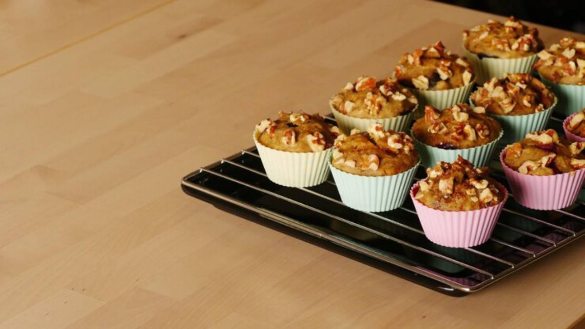 A tray of freshly baked muffins in colorful silicone cups, topped with nuts, resting on a wire rack on a wooden table.