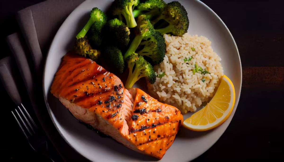 A plated meal featuring grilled salmon, broccoli, and rice, garnished with a lemon wedge on a dark wooden table.