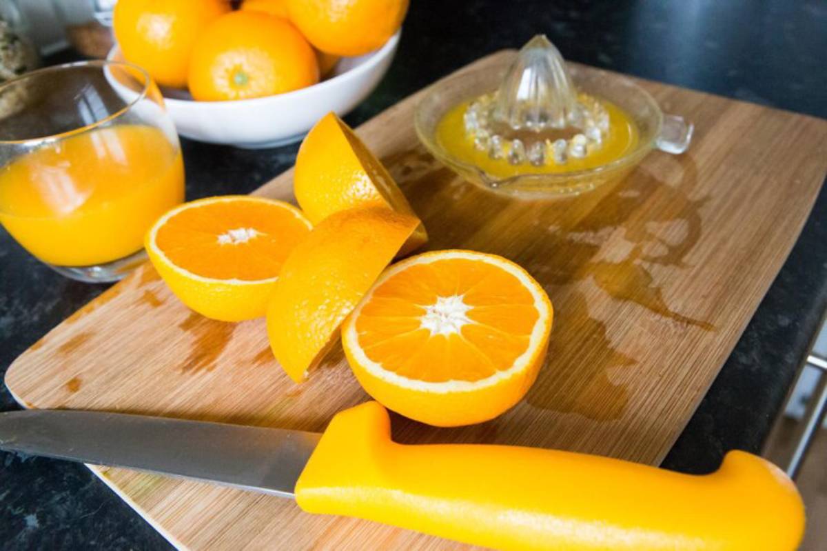 A cutting board with sliced oranges, a glass of orange juice, and a juicer, all showcasing vibrant orange hues.