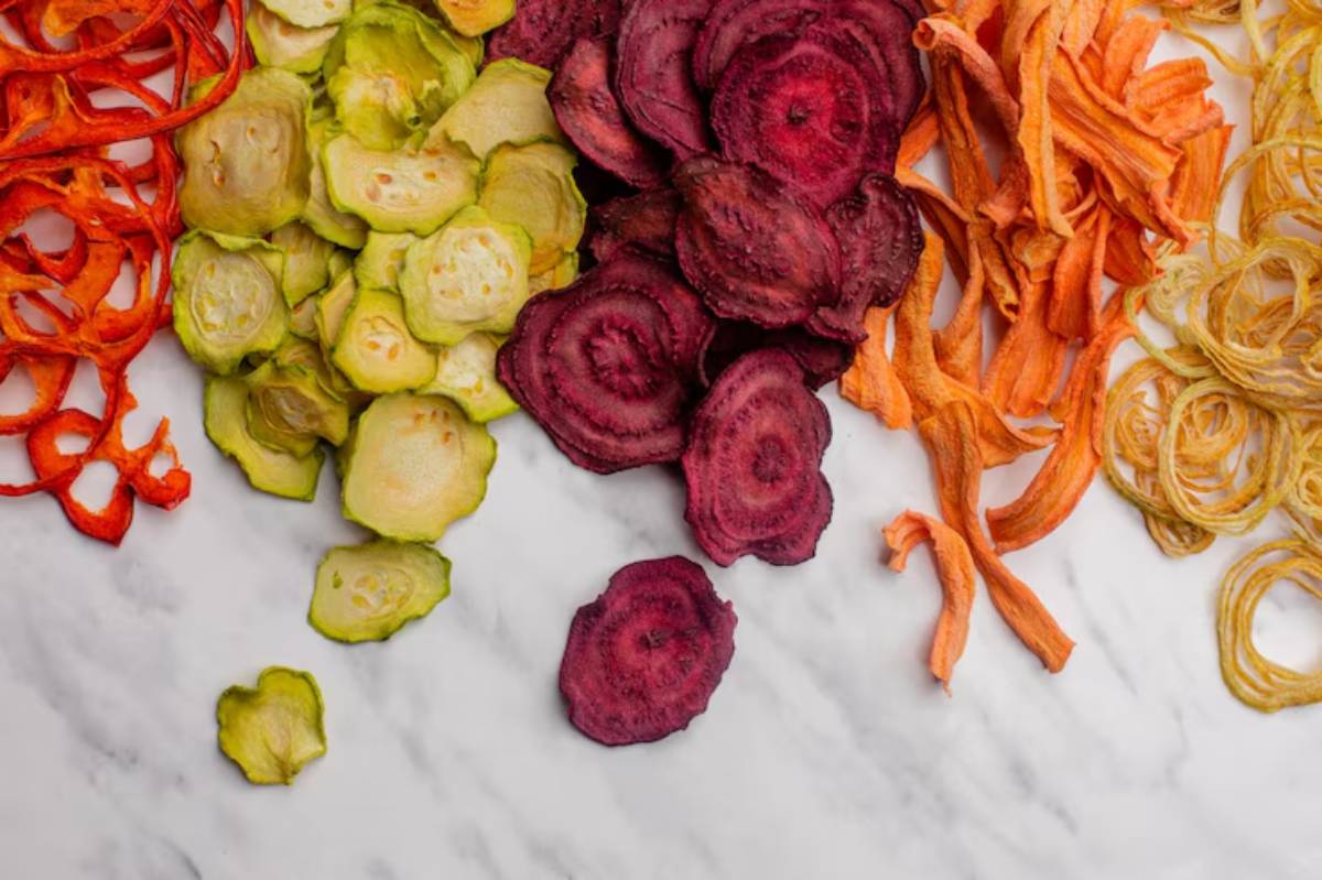 A colorful assortment of dried vegetable slices, including red peppers, green cucumbers, and orange carrots, arranged artistically on a marble surface.