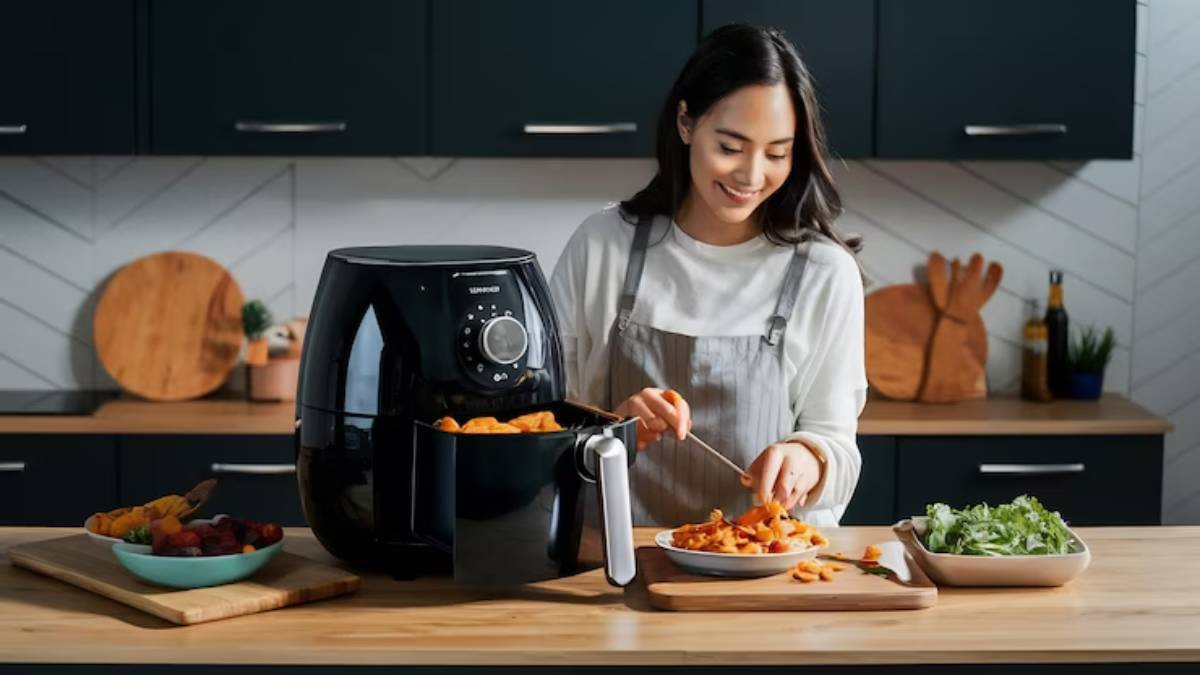 A person in an apron prepares food with an air fryer on a wooden kitchen counter, surrounded by fresh produce and utensils.