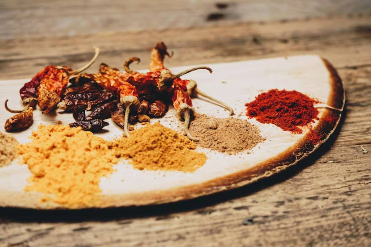 A wooden platter displays a variety of colorful spices and dried chilies, showcasing different textures and earthy tones.