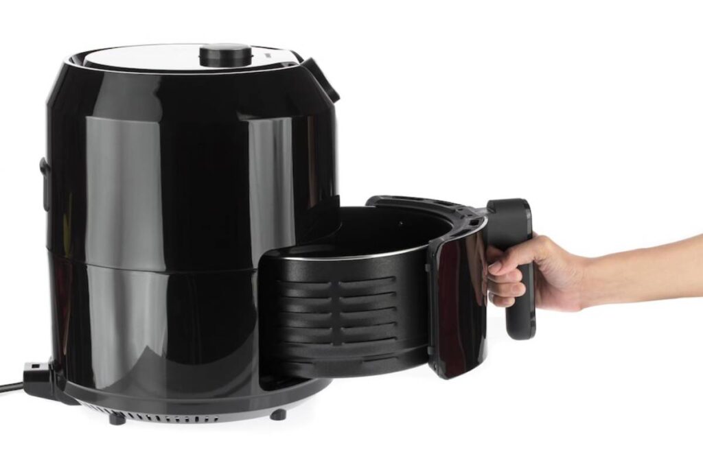 A hand holding the handle of a black air fryer with a removable basket pulled out, showcasing its sleek design and functionality.