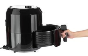 A hand holding the handle of a black air fryer with a removable basket pulled out, showcasing its sleek design and functionality.