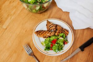 A black plate of golden-brown roasted chicken thighs garnished with fresh basil and roasted garlic on a dark wooden table.