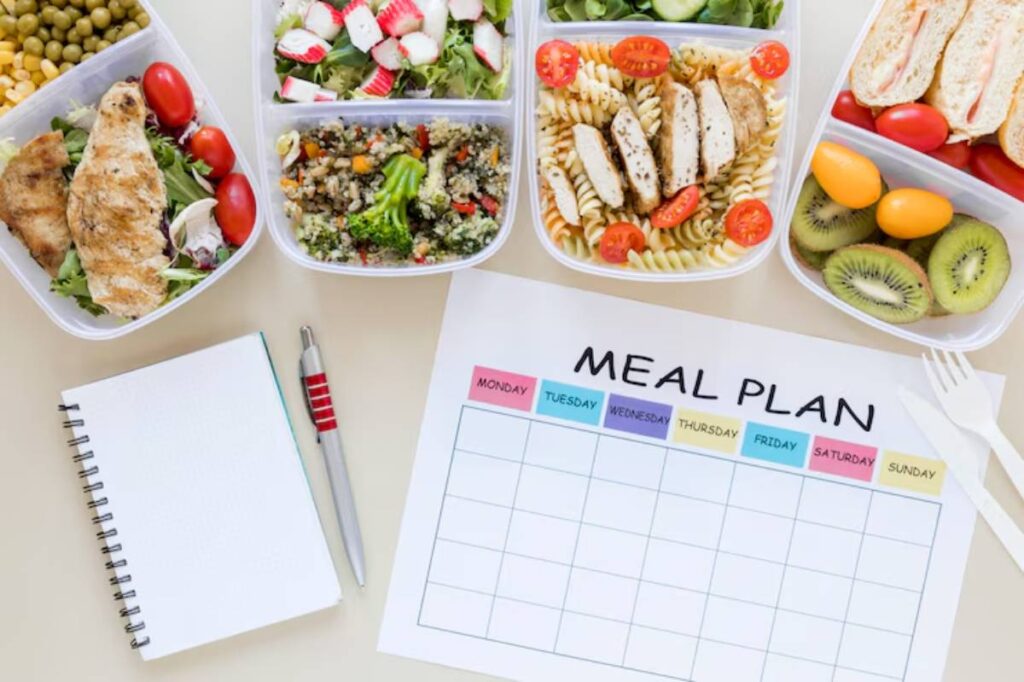 Healthy meal prep with multiple containers of salads, grains, and protein, alongside a blank meal plan chart and notepad.