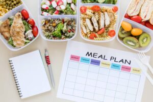 Healthy meal prep with multiple containers of salads, grains, and protein, alongside a blank meal plan chart and notepad.