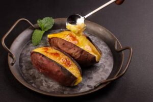 Two roasted sweet potatoes topped with golden custard, served on a metallic plate with a mint leaf for garnish.